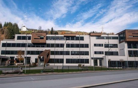 Schulzentrum Taxenbach bei klarem Himmel, modernes Gebäude mit Spielplatz.